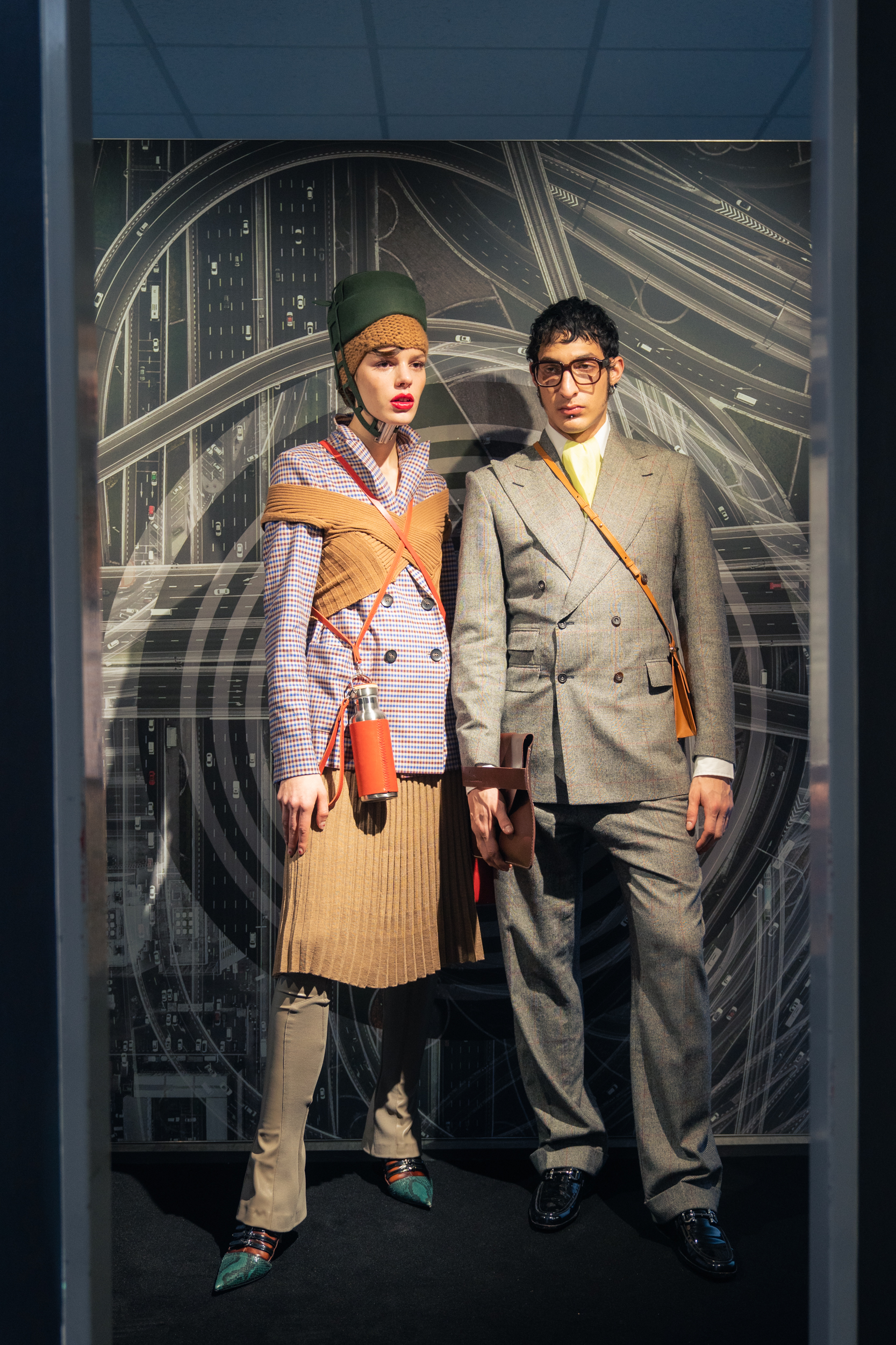 Two models wearing a blazer by Lanius, trousers & skirt by Fassbender, top by Studio Fantastique, knitted hat by Pugnat, hat by Spatz Hutdesign, bag & bottle by Trakatan, handbag by Alexandra Svendsen and shoes Miu Miu at Nightboutique Archive as well as a suit, handkerchief & collar by Maximilian Mogg, shirt by G-Star Raw, clutch by Agnes Nordenholz, crossbody bag by Alinaschuerfeld, glasses by Andy Wolf and shoes by Salvatore Ferragamo Vintage at Neonyt Installation