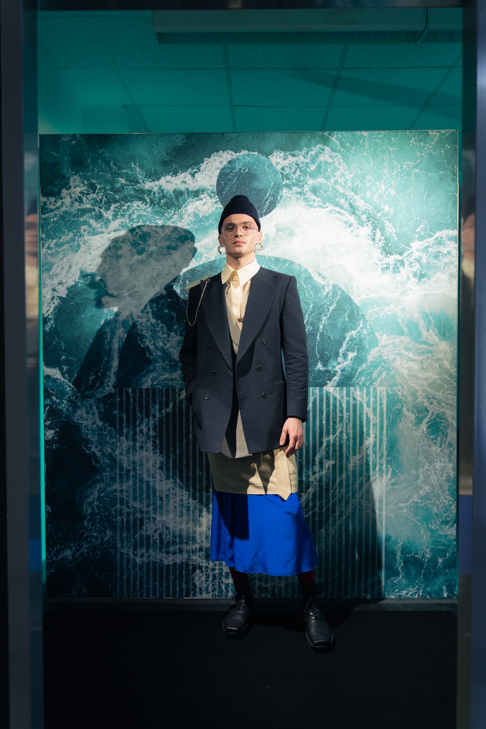 A model wearing a blazer by Maximilian Mogg, shirt by Brachmann, dress by Bav Tailor, skirt by Antonia Zander, Brooch by Gianfranco Ferrè at A.N.G.E.L.O Vintage, necklace by Pulva Jewelry, glasses by mykita, hat by Spatz Hutdesign, socks by Falke and shoes by Trippen at Neonyt Installation